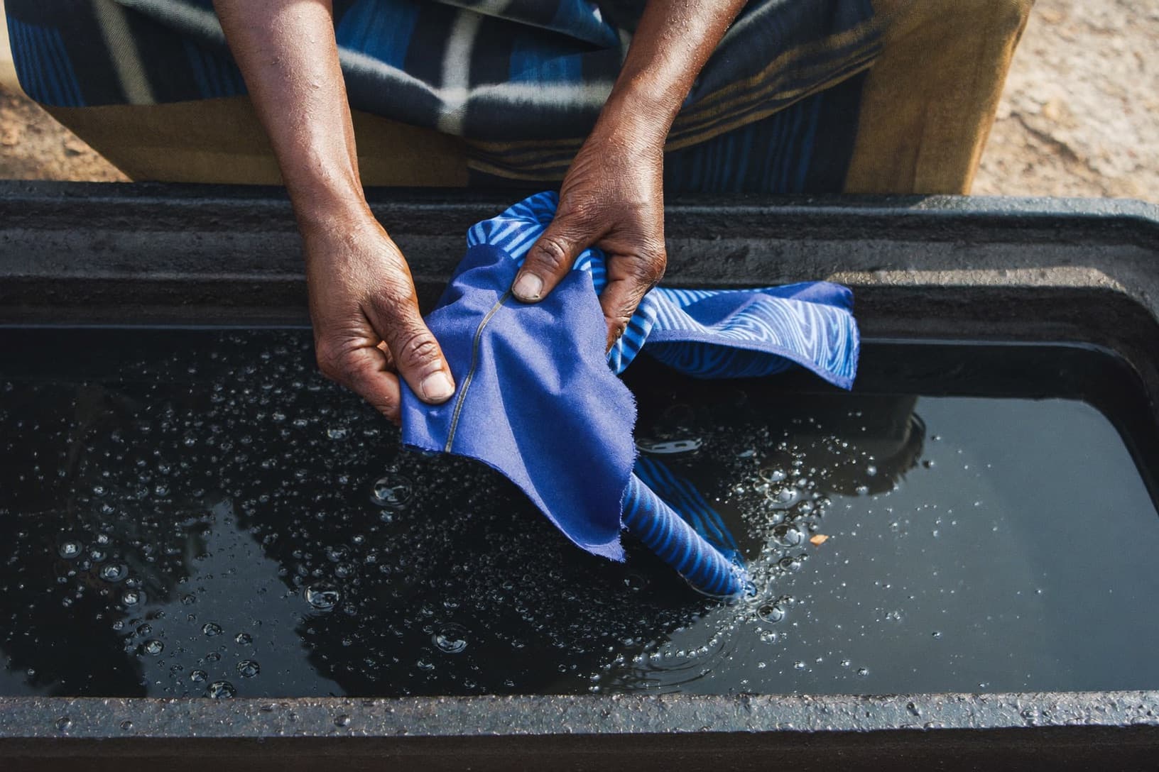 Artisan hands lifting indigo-dyed adire fabric