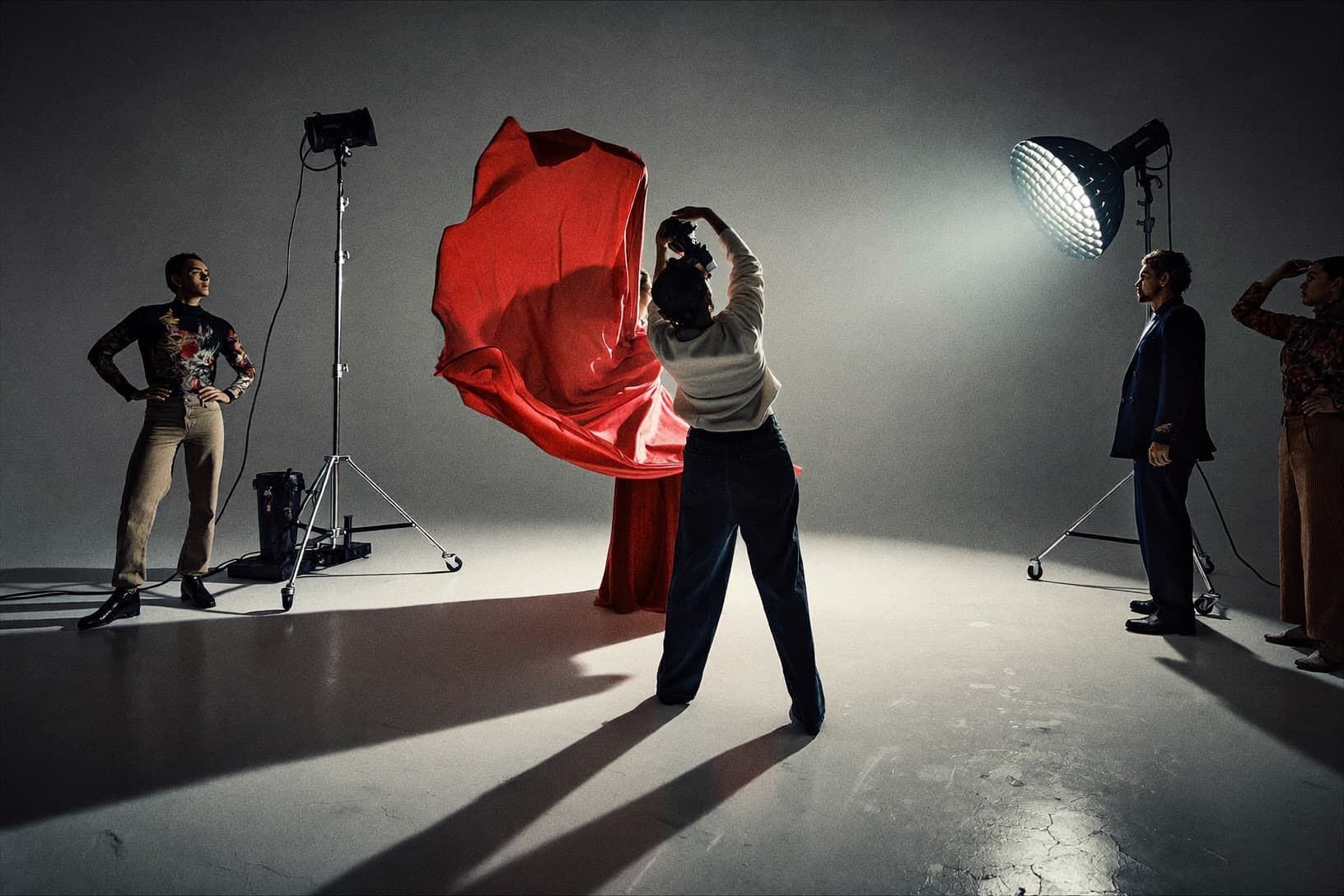 A model in a red gown stands under studio lights between crew and equipment.